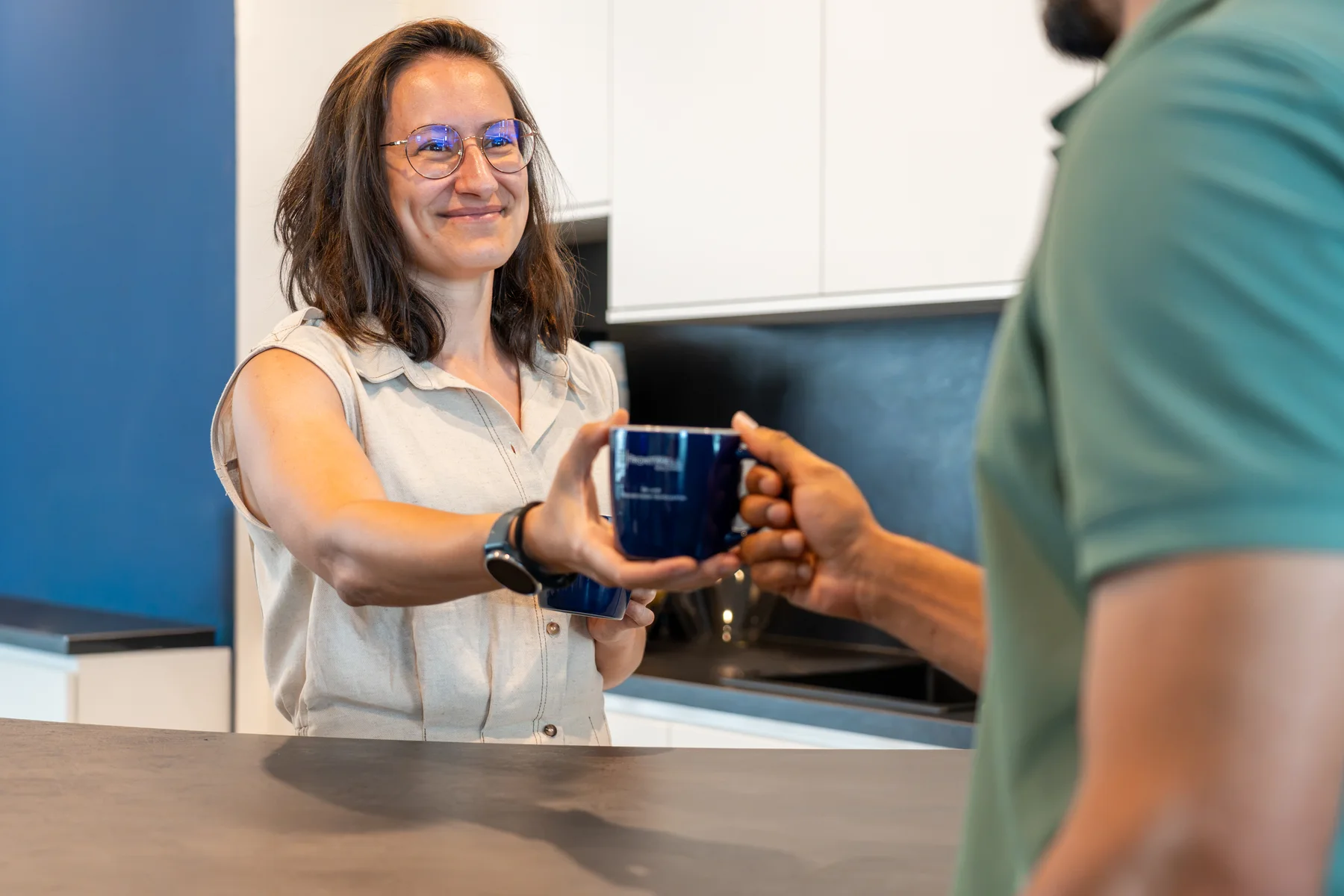 A FrontWell colleague smiling while handing a mug across the office kitchen counter.