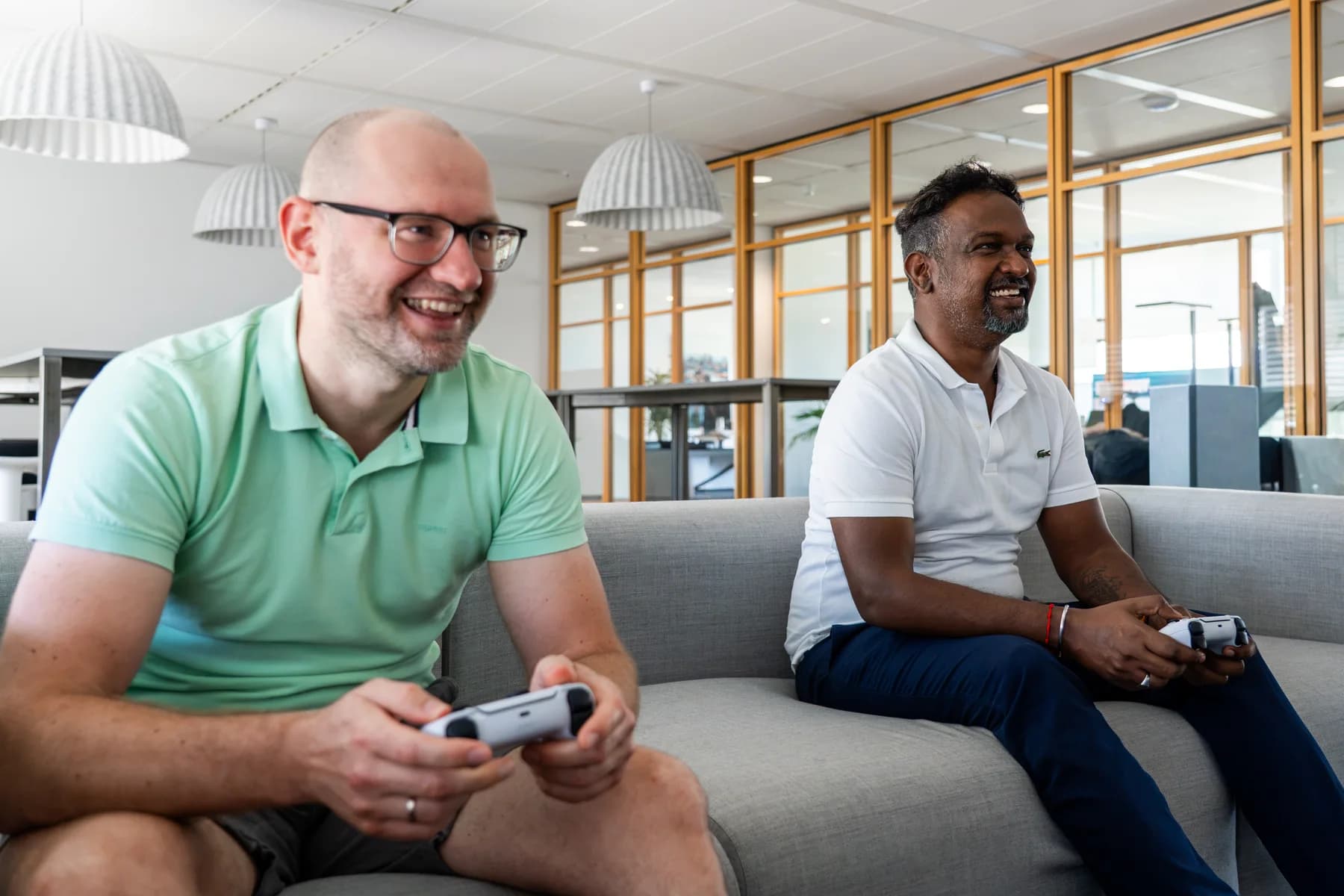 Two FrontWell colleagues relaxing and laughing while playing a video game on a sofa.