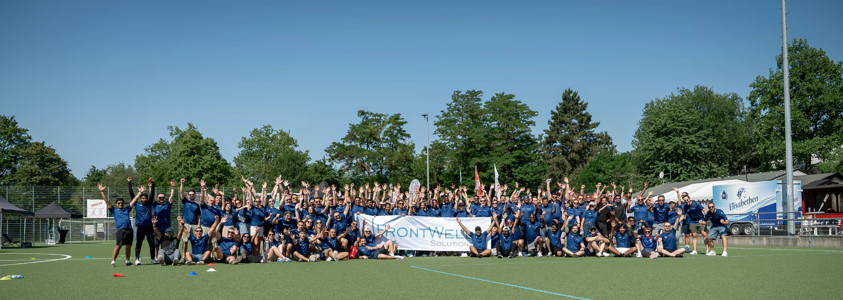 The FrontWell team together at an outdoor event, gathered around a FrontWell Solutions banner.
